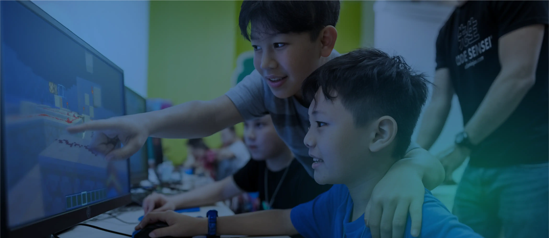Two young boys pointing at a computer monitor displaying a block-based video game